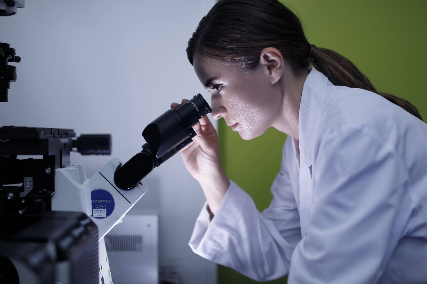 eine Frau mit Pferdeschwanz schaut in ein Mikroskop