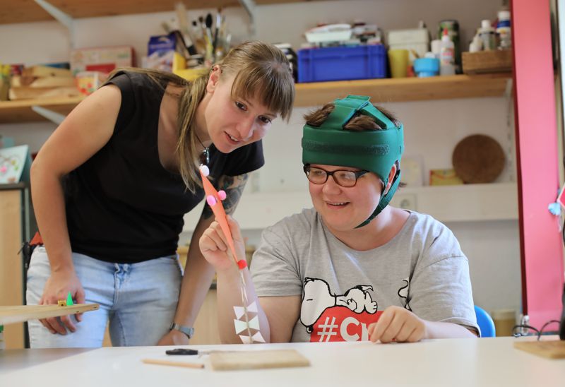ein Kind sitzt am Tisch und arbeitet während eine Frau über seine Schulter schaut