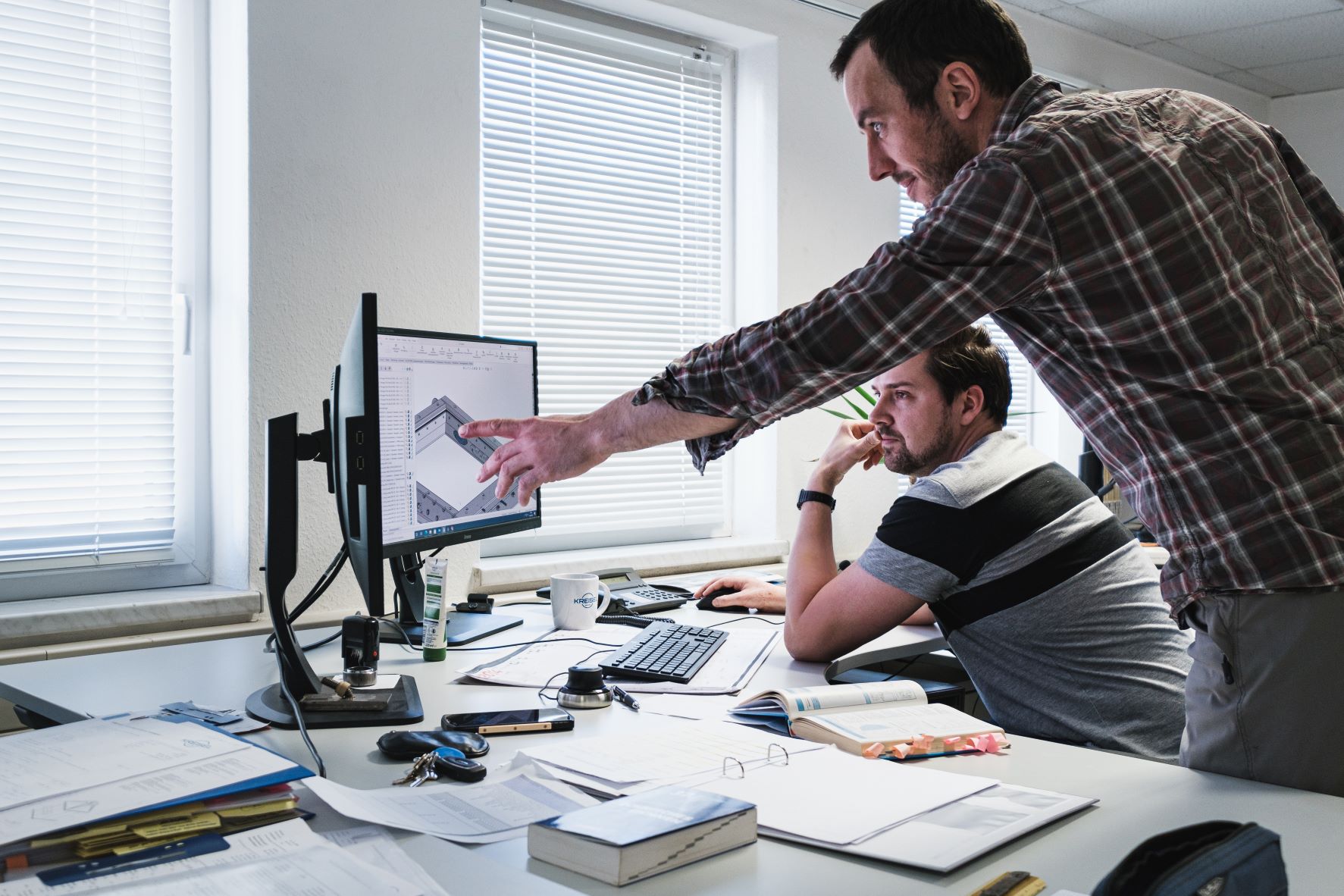 zwei Männer sitzen an einem Schreibtisch vor einem Computer